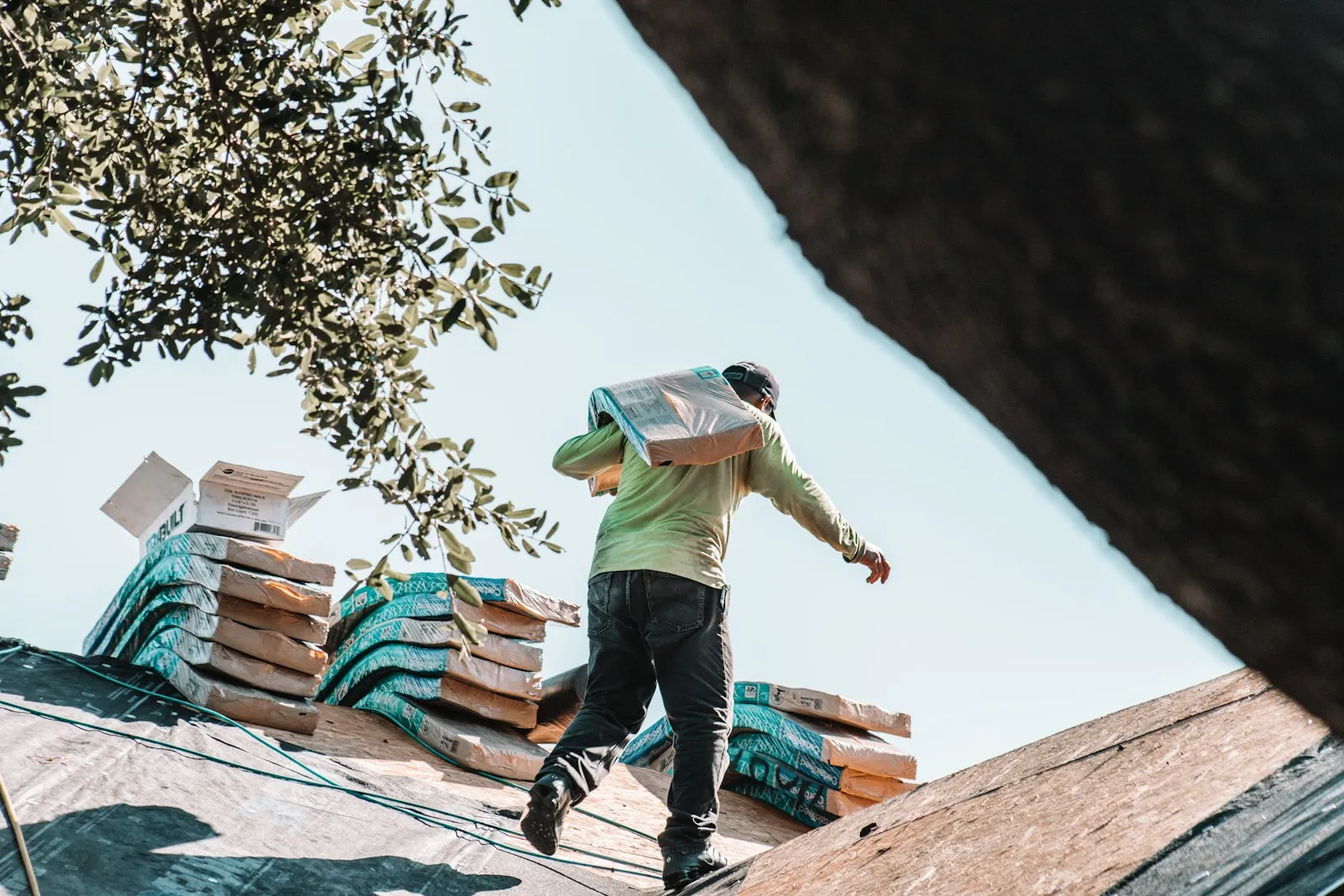 A roofer carrying a bundle of shingles across a roof.